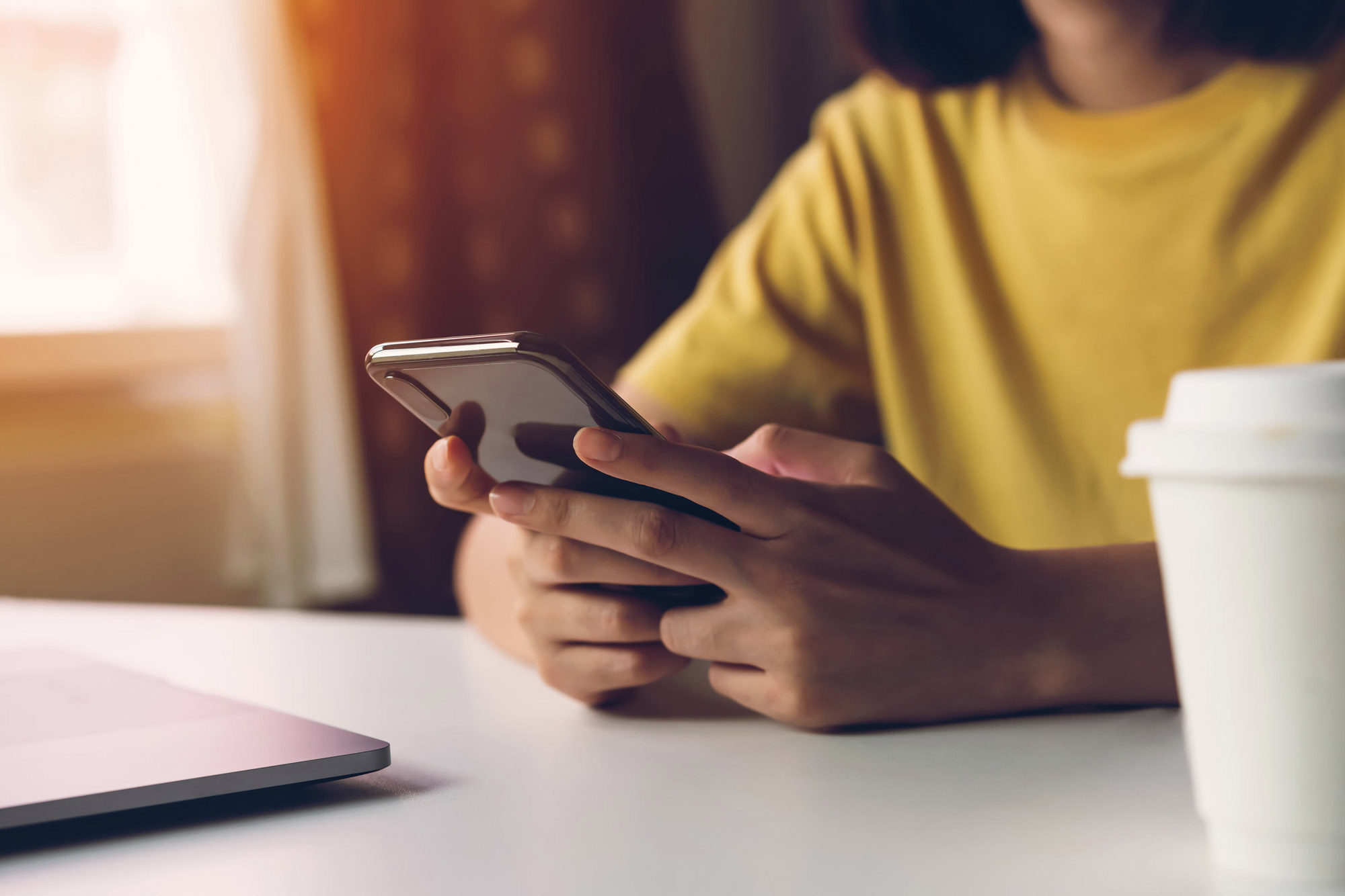 Woman in yellow shirt texting while drinking coffee