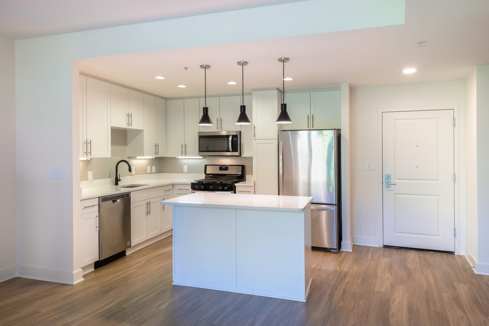 white kitchen shot with island, white cabinets and countertops, stainless steel appliances, black pendant lighting and single basin sink